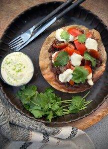 This Slow Cooked Beef Cheek Tostada is a rich, melt in the mouth Mexican-inspired feast. Serve with lime crema on a crunchy tostada base.
